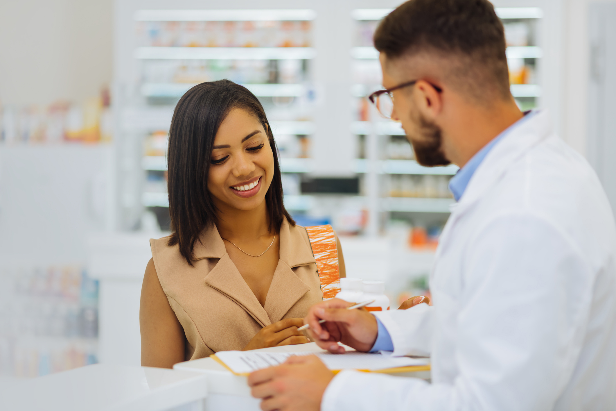 Beautiful international client listening to young apothecary Dark-haired female. Cheerful girl expressing positivity while looking at prescription