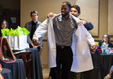 Dr. Kevin Mangat helps Dr. Haneef Muhammad put on his white coat during a party in June 2025 to congratulate those graduating from the Sollus Northwest Family Medicine Residency and welcome new residents to the program. Dr. Mangat will graduate from the program in June 2027, and Dr. Muhammad will graduate in June 2028.  