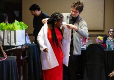 Dr. Ivan Cruz helps Dr. Mandelise Laudat put on her white coat during a party in June 2025 to congratulate those graduating from the Sollus Northwest Family Medicine Residency and welcome new residents to the program. Dr. Cruz will graduate from the program in June 2027, and Dr. Laudat will graduate in June 2028.  