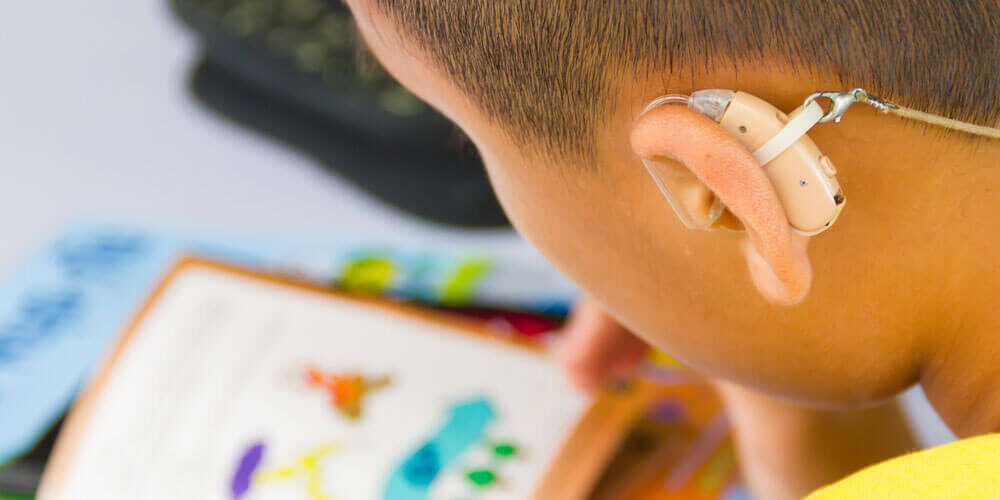 Young boy with a hearing aid reading books