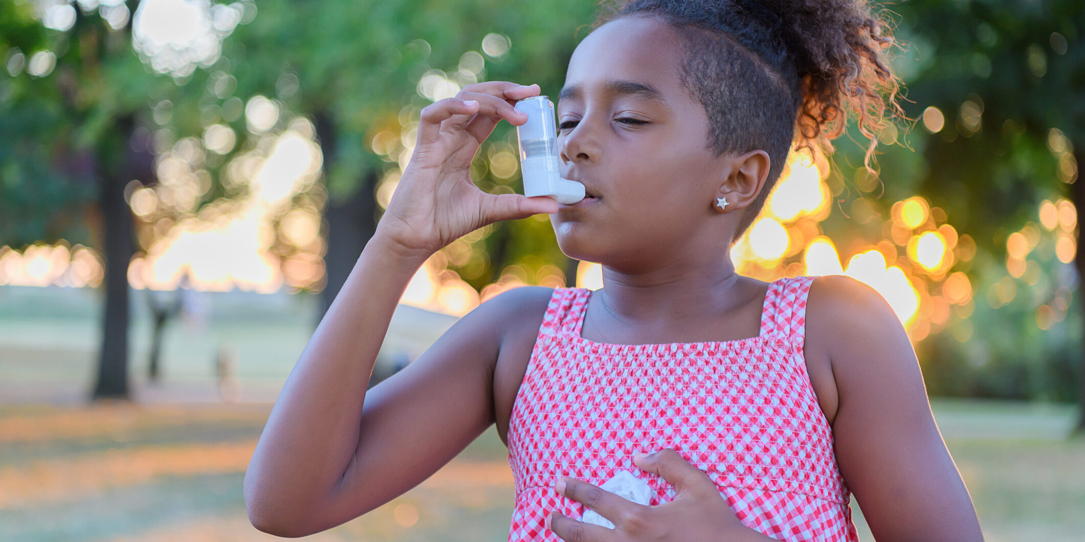 Young Girl of African-American Ethnicity is Using Inhaler Due to the Problems with Asthma in the Public Park.