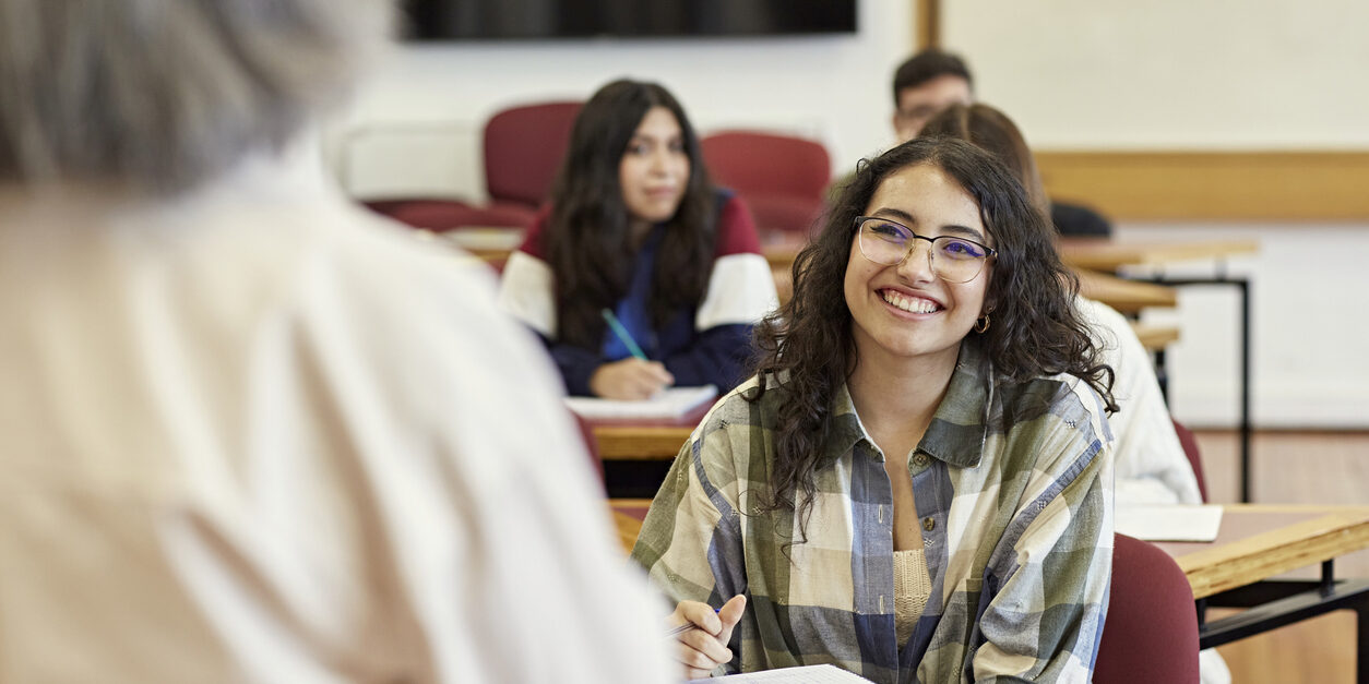 Over the shoulder view with focus on young woman sitting in front row of college classroom, enjoying the lecture and taking notes. Property release attached.