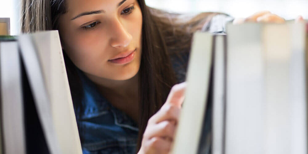 Teenaged girl searching for a book on a library shelf