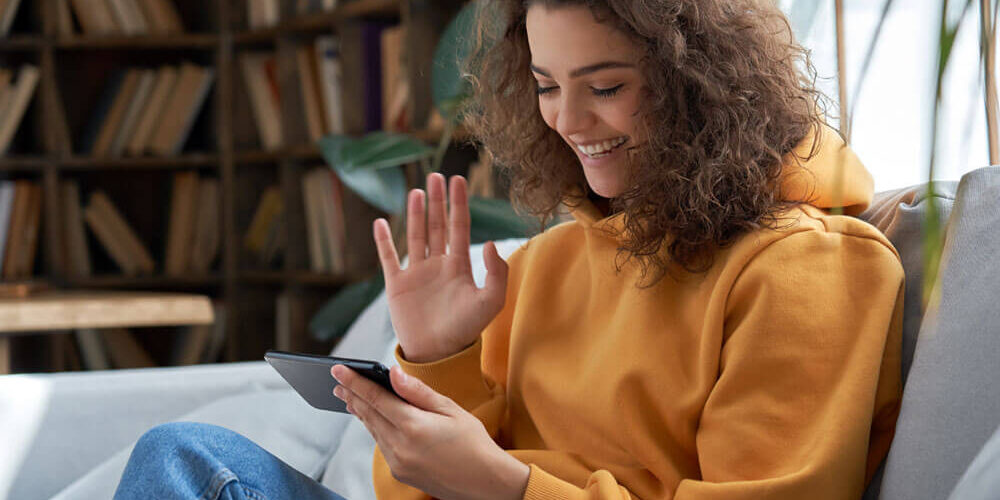 Teenaged girl sitting on a sofa using video chat on cell phone