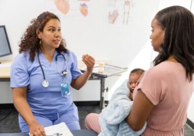 The mature adult female doctor gestures as she gives the young adult mom with a new baby some advice.