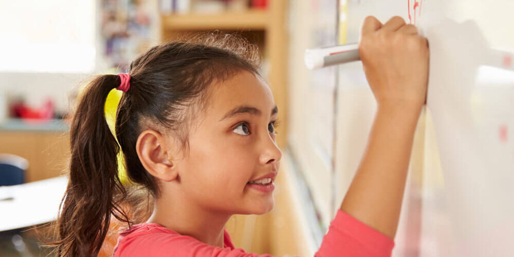 Young girl concentrating as she writes on a whiteboard in a classroom